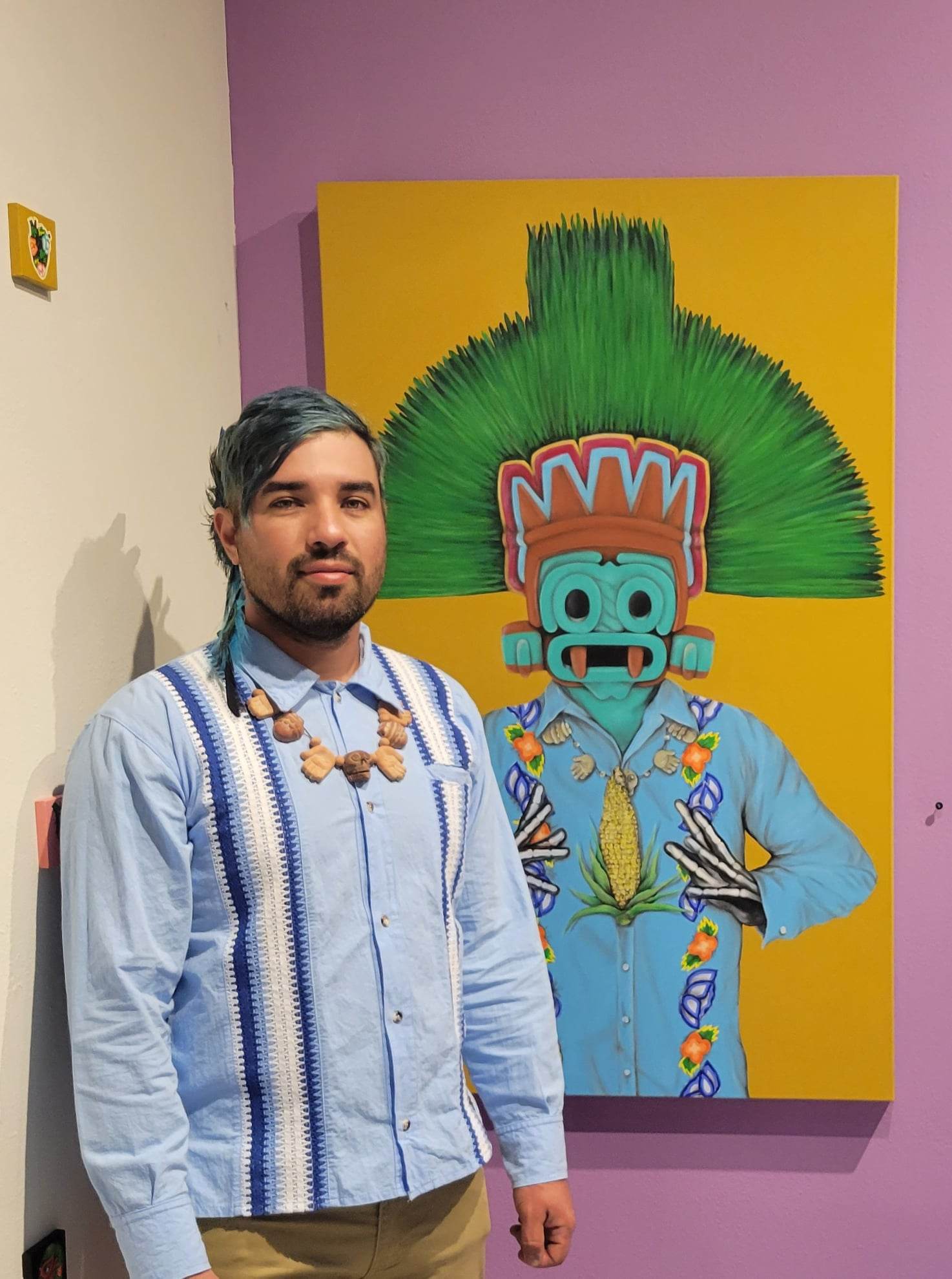 artist Luis Coss standing in front of a brightly colored, Mayan inspired figurative painting